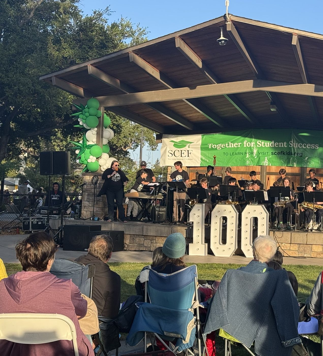 A student jazz band playing at a park bandstand for a seated crowd